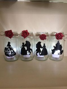 four glass jars with red roses and silhouettes on them, sitting on a counter