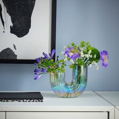 two vases filled with flowers sitting on top of a white table next to a painting