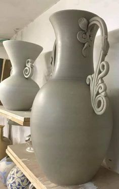 three vases sitting on top of a table in front of a shelf filled with pottery