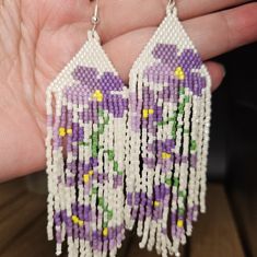 a pair of purple and white beaded earrings with flowers hanging from it's sides