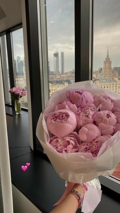 a person holding a bouquet of pink flowers in front of a window with cityscape