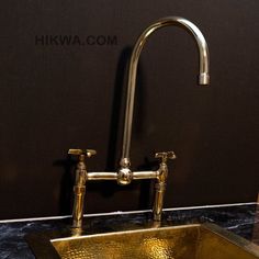 a gold sink with two faucets on the side and a black wall behind it