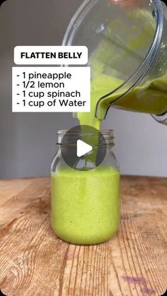 a person pouring green liquid into a glass jar on top of a wooden table with the words flatten belly below it