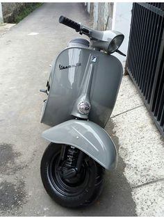 a grey scooter parked on the sidewalk next to a fence