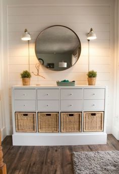 a white dresser with wicker baskets under a round mirror on the wall above it