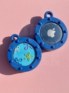 two small blue objects on a pink surface with an apple logo in the middle one