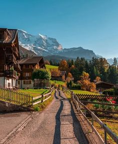 a road that has some houses on it and mountains in the background with snow - capped peaks