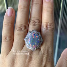 This remarkable Platinum Vintage Ring features a rare large black opal as its center piece. This specimen has a very even medium sized splashes of bright reds blues and greens play-of-color! The black opal is surrounded by a fancy floral like diamond pattern designs. Ring Size: 6.25 Total Weight: 15.75 grams Face Size: 1.1 inch x 0.9 inch Precious Metal: Platinum Precious stones: -Black Opal Center Stone: 6.17 carats, 18.1mm x 13.1mm -White Round Diamonds 0.78 carats Hallmark: Pt900 6.17 D0.78 Formal Multicolor Opal Ring, Multicolor Oval Opal Ring For Formal Occasions, Formal Multicolor Opal Gemstone Ring, Formal Multicolor Opal Jewelry, Gia Certified Oval Cabochon Jewelry Gift, Oval Opal Jewelry Collectible, Collectible Oval Opal Jewelry, Collectible Opal Gemstone Ring, Collectible Opal Jewelry With Gemstones