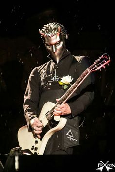 a man with makeup playing an electric guitar in the dark, wearing a mask on his face