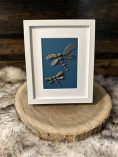 a dragonfly is framed in a white frame on top of a tree stump with beads