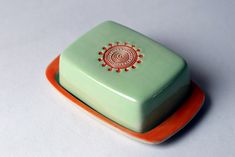 an orange and green plate with a small square shaped object on it's side