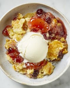 a white bowl filled with fruit cobbler and ice cream sitting on top of a marble counter