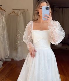 a woman in a white dress taking a selfie with her cell phone while wearing a wedding dress