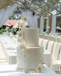 a wedding cake with white flowers and pearls on the top is sitting on a table