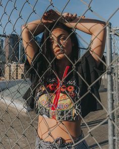 a woman is standing behind a fence with her hands on her head and looking at the camera