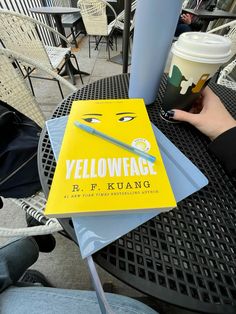 a yellow book sitting on top of a black table next to a cup of coffee