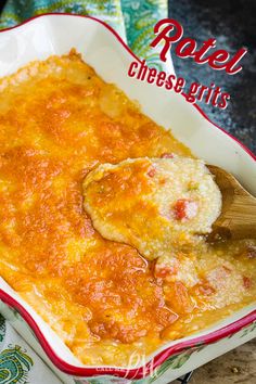 baked cheese grits in a red and white casserole dish with a wooden spoon