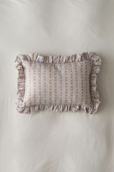 a pillow with ruffled edges on a white bed sheet that has been made into a decorative pillow case