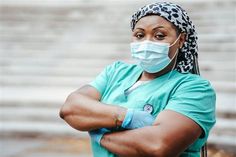 a woman wearing a surgical mask and gloves with her arms crossed looking at the camera