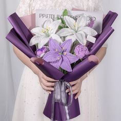 a woman holding a bouquet of white and purple flowers, wrapped in purple satin ribbons