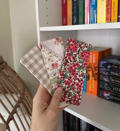 a person holding three pieces of fabric in front of a book shelf filled with books