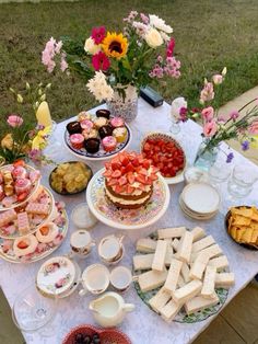 a table topped with lots of food on top of a white table covered in flowers