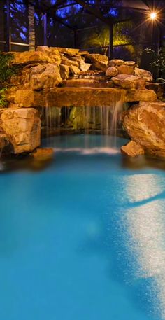 an outdoor pool with waterfall and rocks at night