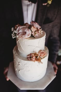 a close up of a wedding cake with flowers on it's top and groom in the background