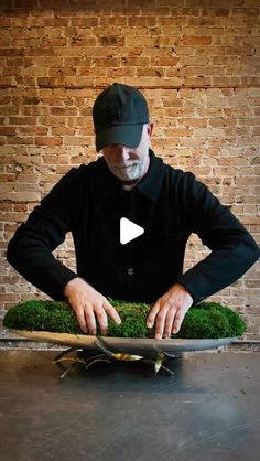 a man in black shirt and hat standing next to a plate with moss on it