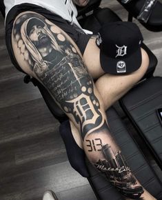 a man sitting on the floor with his leg covered in tattoos and holding a hat