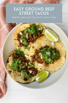 three tacos on a plate with limes and cilantro in the background