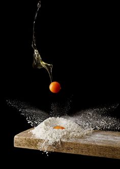 an orange being tossed into flour on top of a cutting board with water splashing from it