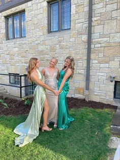 three women in long dresses standing next to each other on the grass near a building