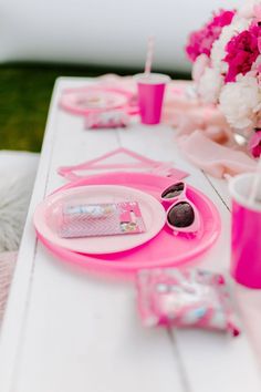 the table is set with pink and white flowers, sunglasses, napkins, and other items