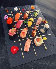 sushi is arranged on a black plate with chopsticks and garnishes