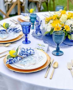 the table is set with blue and white plates, silverware, and yellow flowers