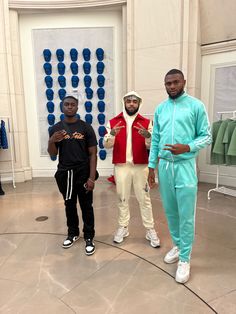 three men standing in front of a wall with clothing hanging on it's walls