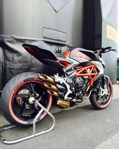 an orange and black motorcycle parked in front of a metal structure on the side of a road