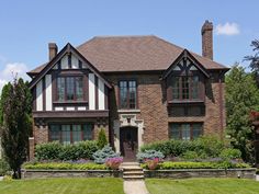 a large brick house with lots of windows and plants in the front yard on a sunny day