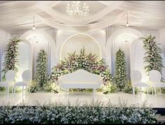 a white couch sitting under a chandelier covered in flowers and greenery next to chairs