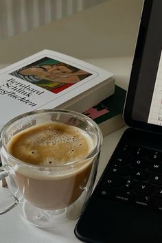 a laptop computer sitting on top of a table next to a cup of coffee and a book