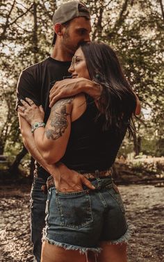 a man and woman embracing each other in front of some trees with tattoos on their arms