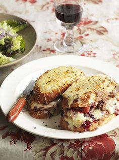 a plate with two sandwiches and a glass of wine on the table next to it