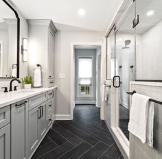 a large bathroom with gray cabinets and black tile on the floor, along with a walk in shower