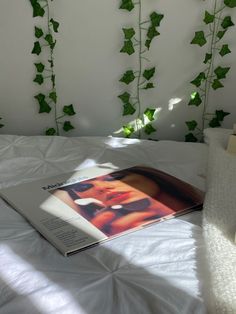 an open magazine sitting on top of a bed next to ivy covered walls and white sheets