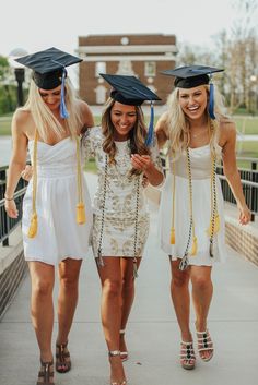 three young women in graduation gowns walking down a sidewalk with tassels on their heads