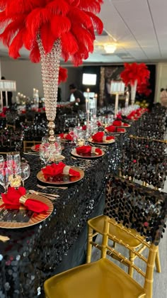 a table set up with red and gold place settings, black sequins and feathers