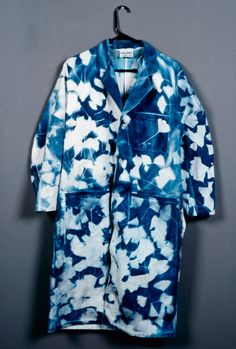 a blue and white tie - dye coat hanging on a hanger against a gray wall