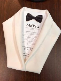 a white jacket with a black bow tie and menu on the front, sitting on a wooden table