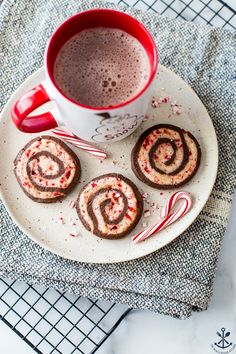 hot chocolates and candy canes on a plate next to a cup of coffee